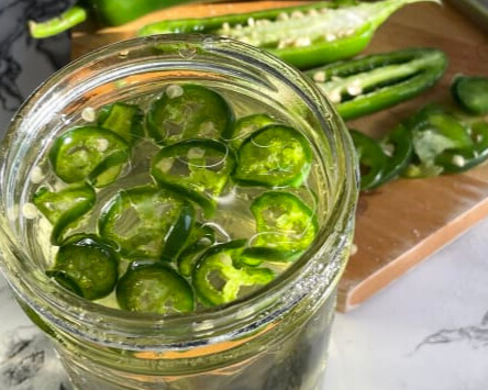 A glass jar filled with homemade Jalapeno Simple Syrup, showcasing fresh jalapeno slices infused in a sweet syrup, perfect for adding a spicy kick to cocktails and beverages
