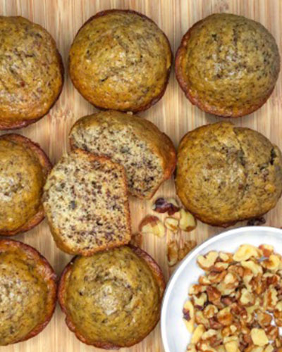 Homemade banana nut muffins fresh from the oven, with golden-brown tops and scattered chopped nuts on a rustic wooden surface. A delightful treat for breakfast or a snack.